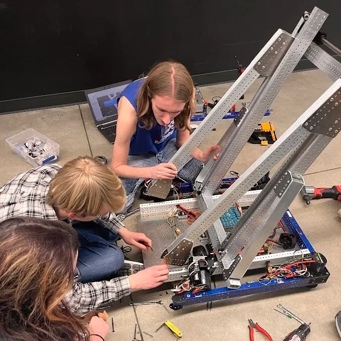 Three teenagers from Generals Robotics assembling a large robot